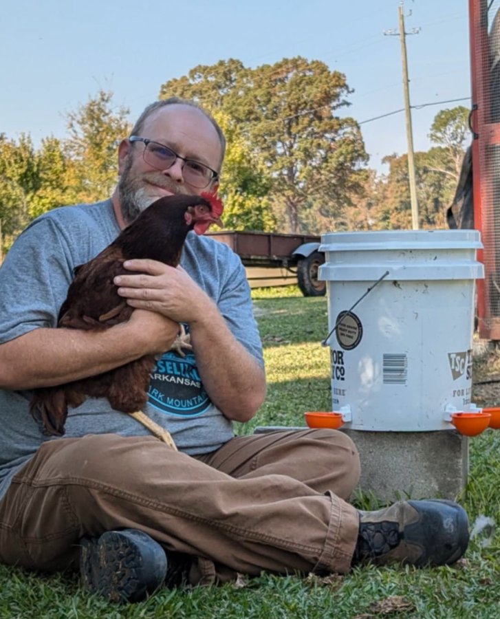 Customer photo: a keeper holding a hen beside a bucket fitted with Lil'Clucker waterer cups