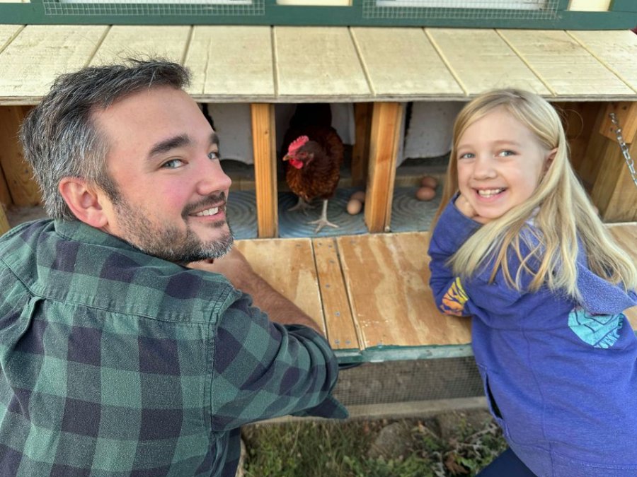 Customer photo: a keeper at his coop, a hen settled on a Lil'Clucker nesting pad behind him